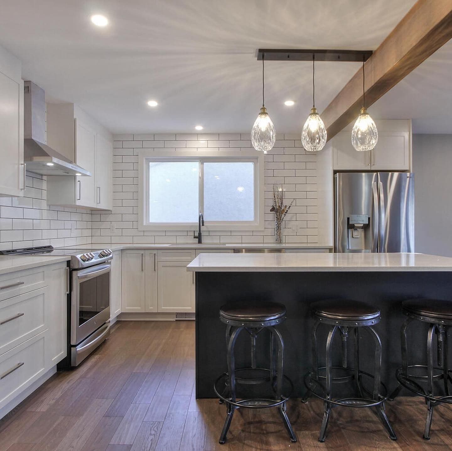 An island with a dark base, pendant lights and a wood beam — Fulton Place