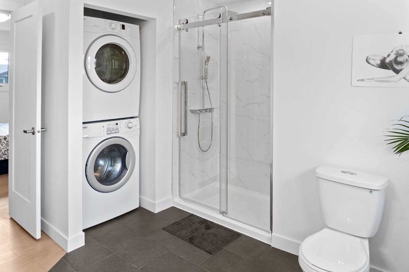 A bathroom with a walk-in shower and stacked washer and dryer